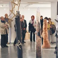 V središču galerije gozd dreves, ki se prepleta z  žensko  