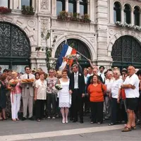 Skupinska fotografija svatov in prijateljev pevcev iz tržaškega pevskega zbora na osrednjem tržaškem trgu; v ozadju plapola  jugoslovanska zastava z rdečo zvezdo.
