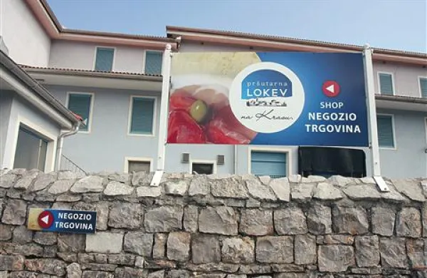 “Negozio/trgovina” piše na usmerjevalni tablici na zidu ob lokavski pršutarni, na veliki tabli nad njim pa je slovenščina na zadnjem mestu. Za Lokavce so napisi sporni, za pristojnega inšpektorja ne.