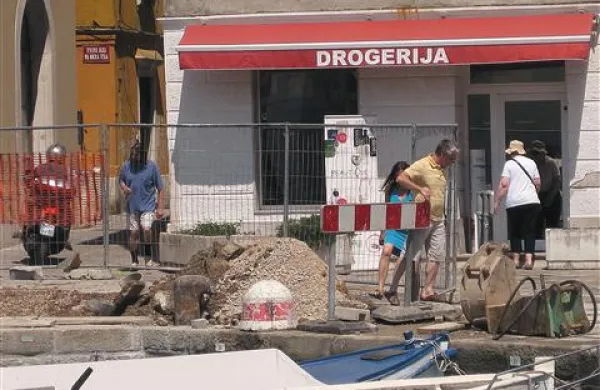 Turisti  zatavajo na gradbiščni gramoz, med nedokončane jaške in na pol prekrite cevi