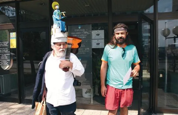 Brecelj je včeraj prišel na sodišče s kitaro, kamero in klobukom s podobo Borisa Popoviča, pa so mu varnostniki pobrali kamero in kitaro. S klobukom je hodil po hodnikih sodišča, v sodni dvorani pa mu je sodnik ukazal, naj si ga sname. Desno od njega je Friškič, ki se na sojenje vozi iz Prekmurja.