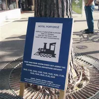 Turistični vlakec svoj vozni red objavlja na leseni tabli, naslonjeni kar na drevo na portoroški promenadi