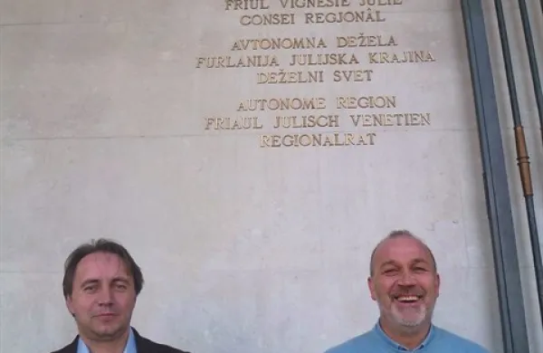 Deželna svetnika Igor Gabrovec in Igor Kocjančič pred sedežem deželnega sveta Furlanije-Julijske krajine v Trstu. Napis ob vhodu je v štirih jezikih: italijanščini, furlanščini, slovenščini in nemščini