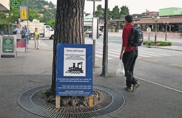 Table z urnikom turističnega vlakca so na postajah kar naslonjene na drevesa in zidove 