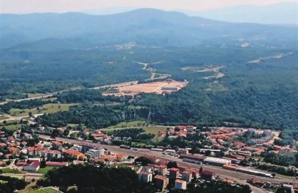 Občina Divača pritiska na Primorje v stečaju, da izpolni svoje obveznosti v industrijski coni Risnik (na fotografiji rjava lisa nad mestom),  da bi potencialni kupcem  v coni lahko ustrezno uredila priključke na infrastrukturo in obračunala komunalni 
