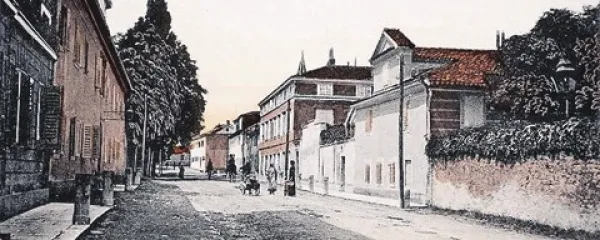 Kolorirana fotografija (iz leta 1910) glavne ulice v Sežani,  na levi strani pogled na hotel Tri krone, na desni vila Scaramanga, danes občinska stavba. Razglednica je last Kosovelove knjižnice Sežana.
