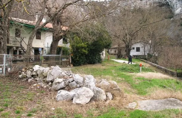 Neasfaltirani del stare poti, ki vodi do hiše in mlina Pavličevih (v ozadju), še vedno prekriva kup kamenja 