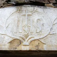 Jezusov monogram z značilnim srcem je svojevrsten podpis kamnoseka Matevža Guština -  Celana iz Griž. Na fotografiji vhodni portal Hribovih v Stomažu na Vrheh.