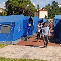 Začasno šotorišče na nekdanjem nogometnem igrišču nudi bistveno boljše bivanjske pogoje od “džungle” ob Soči.