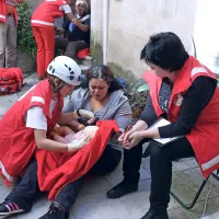 Na dvorišču palače Carli so reševalce čakali pretreseni  člani družine, ki so preživeli hud potres. Na fotografiji reševalka pomaga dojenčku, ki ga drži pretresena mama, ob njima pa sedi ocenjevalka.