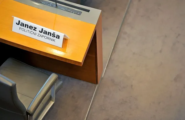 anša sicer ni prisoten v razpravni dvorani, na njegovem sedežu pa piše “Janez Janša, politični zapornik”