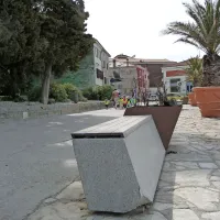 Okrasno rastlinje je posušeno, betonski klopi pa manjka en    
vogal.  

