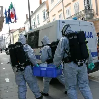 Trije gasilci v “vesoljski opravi” se odpravljajo v stavbo 
zapečatit prostore in podučit policista ter tri občinarje o 
načinu dekontaminacije.