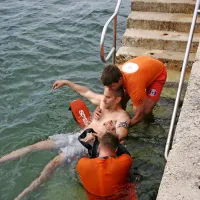 Reševalca s skupnimi močmi spravljata utopljenca iz vode.