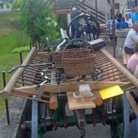 Na dvorišču pa  voz lojtrnik, na njem košare, brana in plug, v 
ozadju slamoreznica.