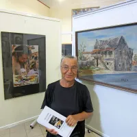 Jožica Zafred, fotografinja in žena pokojnega slikarja Stojana Zafreda,  
med  fotografskim portretom  moža in Stojanovim oljem z motivom 
Škrateljnove hiše.

