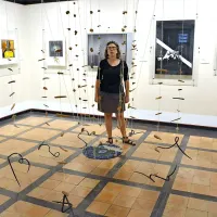 Katarina Brešan ob Pogačnikovi viseči  skulpturi, nastali v času Družine v Šempasu 
(1971-1979). Prepletajo se  štirje elementi: volna, glina, les in železo.  