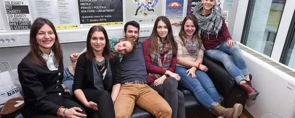 Del ekipe Medijske komune (medijskakomuna.si)  na svojem priljubljenem kavču pod steno s slogani za prihodnost. Z leve: Vera, Darja, Tina  2, Iztok, Klara, Sara in Alenka.  