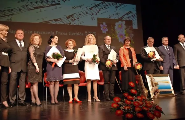 Tamara Ražem Locatelli (v sredini, v beli obleki) med nagrajencema in dobitniki priznanj na podelitvi v Cerknici 