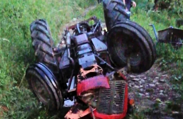 Traktor se je s kolesi v zraku ustavil na kolovozu pod sadovnjakom, 
voznik je obležal tik ob njem. 