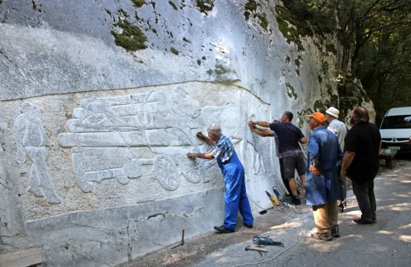Člani  skupine Kamnoseki Manče ob hudourniku Bela izdelujejo  
svojevrsten kamniti relief z upodobitvijo konjske vprege.