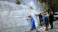 Člani  skupine Kamnoseki Manče ob hudourniku Bela izdelujejo  
svojevrsten kamniti relief z upodobitvijo konjske vprege.