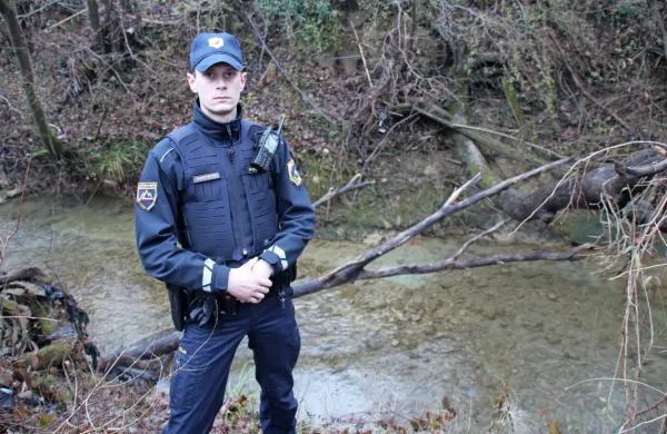Policist Benjamin Franca ob drevesu, ob katerem so reševali 
47-letno migrantsko mater. 