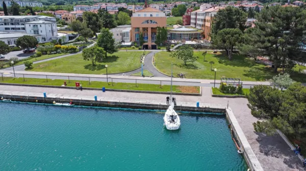 Čeprav je fotografija nastala 19. maja, se od takrat ni veliko 
spremenilo: ob pomolu  E je  namesto  plovil  še vedno videti baraže, 
za njimi pa so še   pivniki in vpojna čreva. V ozadju  je hotel 
Delfin.    