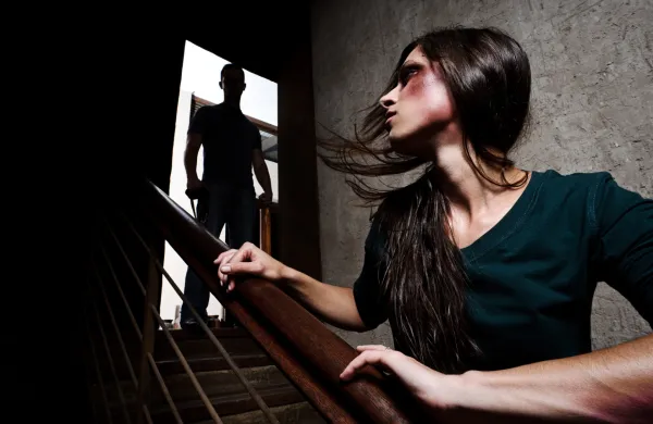 Concept of domestic abuse. Battered woman escaping from man silhouetted at the top of the stairs, in fear of more violence NASILJE NAD ŽENSKAMI