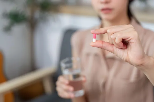 A young woman holds a capsule in one hand and a glass of water in the other, ready to take her medication. Focus on health management.,Image: 1018421167, License: Royalty-free, Restrictions:, Model Release: no, Credit line: Worawee Meepian/Alamy/Profimedia