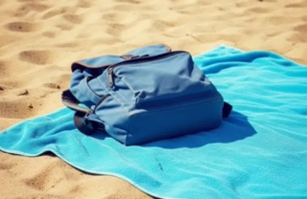 Pe&scaron;čena plaža v mirnem poletnem dnevu.Brisača razgrnjena na toplem pesku.Nahrbtnik pripravljen ob počitku ob morju.