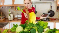 Young woman in kitchen having many green vegetables on table, holding tablet thinking about cooking something and searching for recipes in internet. Woman having green vegetables thinking about cooking,Image: 1121011550, License: Royalty-free, Restrictions:, Model Release: no, Credit line: -/Ingram/Profimedia