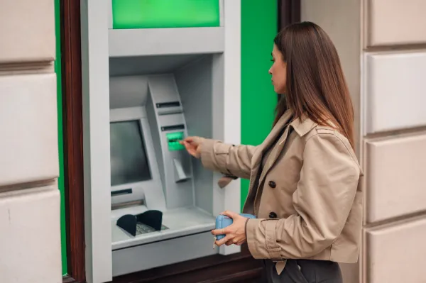 Woman withdrawing cash from an atm on a city street, inserting her card for a secure transaction. Financial independence in a modern urban setting